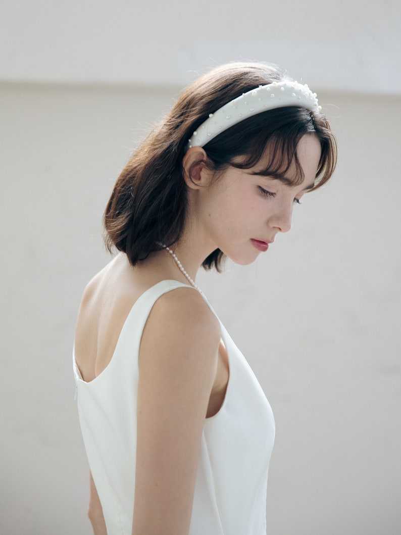May include: A woman wearing a white sleeveless dress with a pearl necklace and a white headband with pearl embellishments.