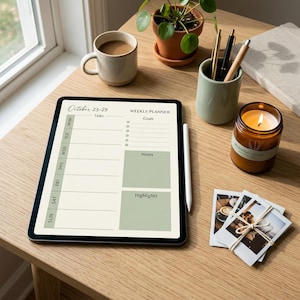 Op de afbeelding: Een digitale weekplanner op een tablet met een stylus, koffiemok, brandende kaars, pennen en een kleine plant op een houten oppervlak. De planner toont de data van 23-29 oktober. Er ligt ook een stapel polaroidfoto's.