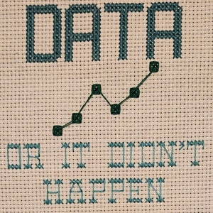 May include: Cross-stitch artwork with the words "DATA" above a green line graph, and the phrase "OR IT DIDN'T HAPPEN" below. The text and graph are stitched in teal thread on a cream-colored fabric.