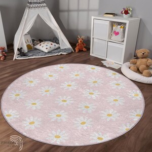May include: A pink round rug with a white daisy pattern. The rug is in a room with a teepee, a wooden shelf, and a stuffed animal.