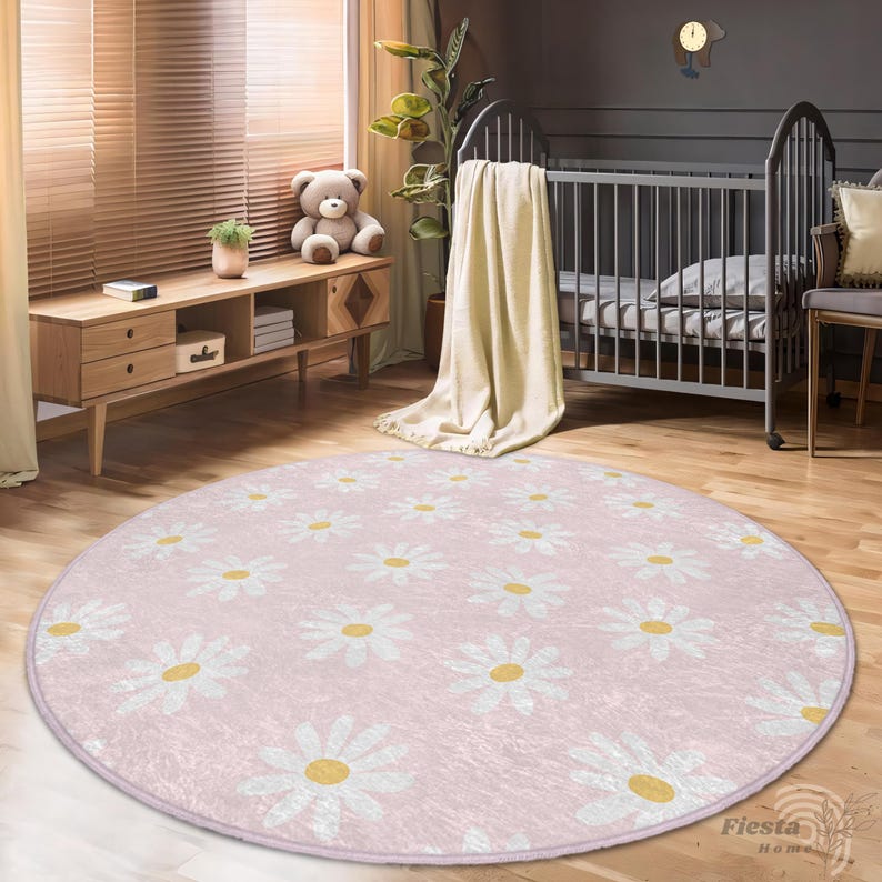 May include: A pink round rug with a white daisy pattern. The rug is in a nursery with a crib and a wooden dresser.