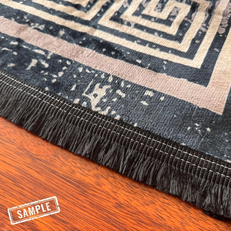 May include: A close-up of a black and white patterned rug with a black fringe border. The rug has a geometric design and is made of a soft, plush material.