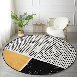Può includere: Un tappeto rotondo con sfondo bianco e strisce bianche e nere. Il tappeto ha un design geometrico con una sezione di colore giallo senape e una sezione nera.