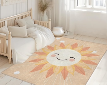 May include: A rectangular area rug featuring a smiling sun design. The rug has a peach background with a large sun in the center, colored in shades of yellow, orange, and white. The sun has a smiling face and is surrounded by radiating lines.