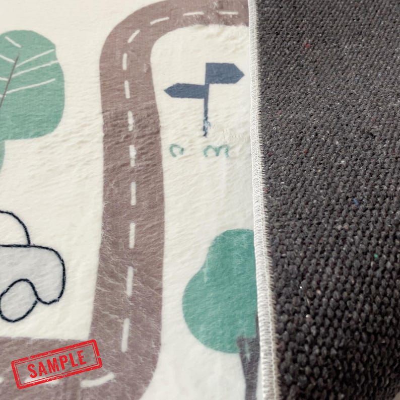 May include: A soft, off-white rug with a road design, trees, and a car illustration. The road is brown with white dashed lines. The rug has a gray border and a red "SAMPLE" stamp.