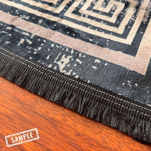 May include: A close-up of a black and white patterned rug with a black fringe border. The rug has a geometric design and is made of a soft, plush material.