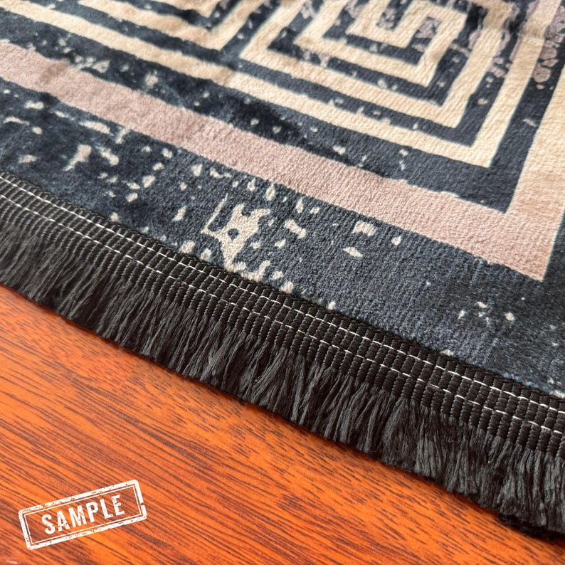 May include: A close-up of a black and white patterned rug with a black fringe border. The rug has a geometric design and is made of a soft, plush material.