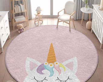 Puede incluir: Alfombra redonda rosa con diseño de unicornio. El unicornio tiene un cuerno dorado, ojos cerrados y una corona floral. La alfombra es de material suave y texturizado, ideal para la habitación de un niño. Diámetro aproximado 150 cm.