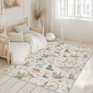 May include: A rectangular rug with a cream background features a repeating pattern of various dinosaurs, palm trees, and ferns in shades of brown, green, and blue. The rug is placed on a light wood floor in a bedroom setting.