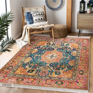 Könnte beinhalten: Ein bunter, gemusterter Teppich mit einem blauen, rosa, gelben und orangenen Design. Der Teppich hat einen weißen Fransenrand und liegt auf einem Holzboden.