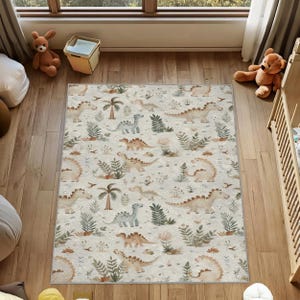May include: A rectangular area rug with a repeating pattern of dinosaurs, palm trees, and foliage in shades of beige, tan, and green. The rug is placed on a wooden floor in a child's room, with a crib and stuffed animals visible.