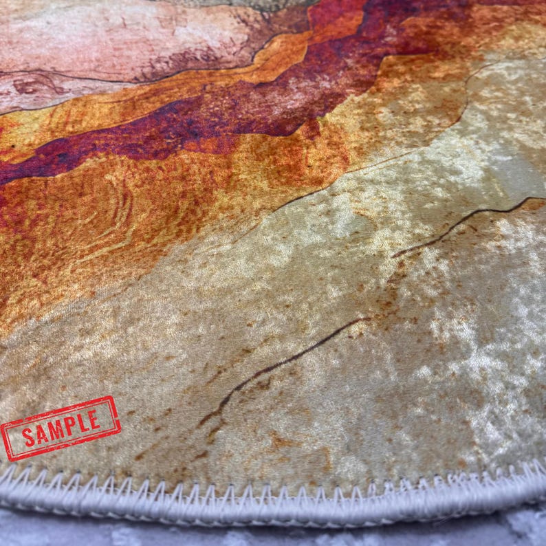a close-up view of a textured surface with a vibrant, abstract pattern in shades of orange, red, and beige. The surface appears to be a rug or carpet, with a red stamp visible in the bottom left corner.