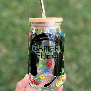 Puede incluir: Un tarro de vidrio transparente con tapa de bamb&uacute; y una pajita de acero inoxidable. El tarro tiene un gr&aacute;fico en blanco y negro de unos auriculares con el texto "GAMER FUEL" en &eacute;l. El gr&aacute;fico tambi&eacute;n incluye s&iacute;mbolos de mando de juego de colores.