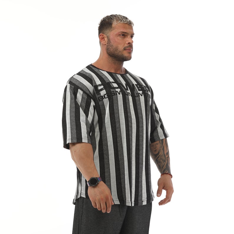K&ouml;nnte beinhalten: Ein schwarz-wei&szlig; gestreiftes T-Shirt mit kurzen &Auml;rmeln und dem Schriftzug "POWER" in Schwarz auf der Vorderseite. Das Shirt hat eine lockere Passform und eine etwas l&auml;ngere L&auml;nge.