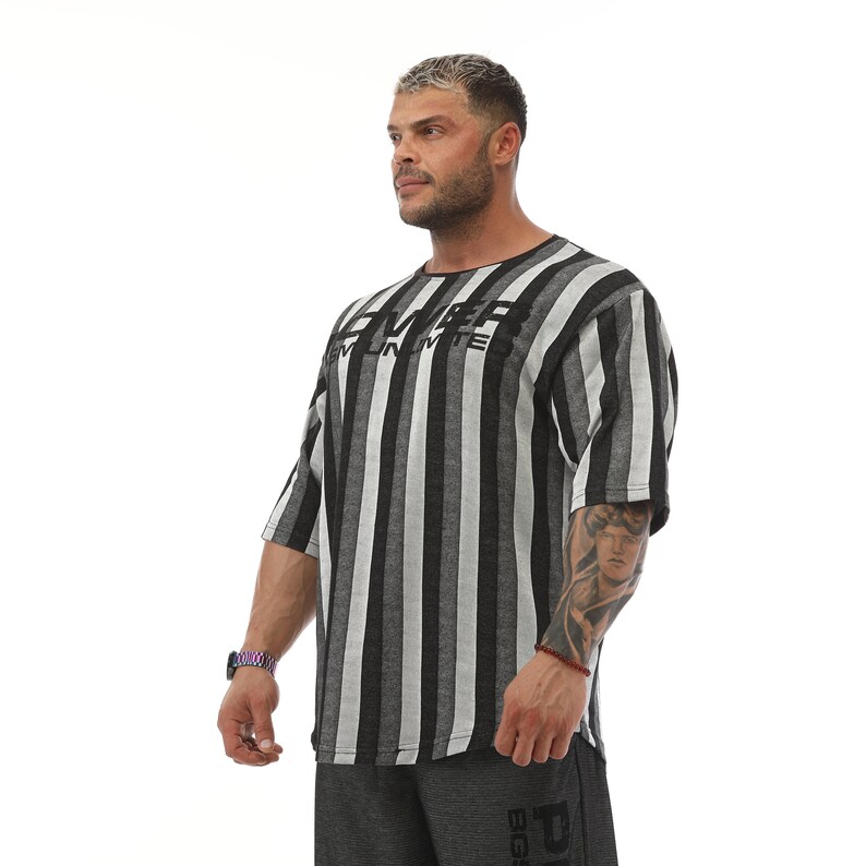 K&ouml;nnte beinhalten: Ein schwarz-wei&szlig; gestreiftes T-Shirt mit dem Aufdruck "EMPEROR" auf der Vorderseite. Das Shirt hat eine lockere Passform und kurze &Auml;rmel.