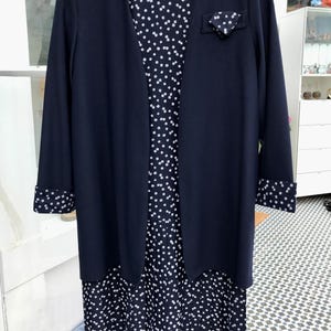 Könnte beinhalten: Ein marineblaues Kleid mit weißem Blumenmuster und eine passende marineblaue Strickjacke. Das Kleid hat einen Faltenrock und die Strickjacke hat eine kleine Tasche auf der linken Seite.