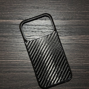 Könnte beinhalten: Schwarze Handyhülle mit einem Karbonfasermuster. Die Hülle hat eine glänzende Oberfläche und eine rechteckige Form mit einem Kameraausschnitt. Das Design zeigt ein sich wiederholendes Muster aus kleinen, reflektierenden Punkten und diagonalen Linien.