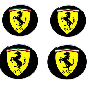 May include: Four black circular emblems featuring the Ferrari logo. Each emblem has a yellow shield with a black prancing horse, the letters "SF" below, and a green, white, and red stripe at the top.