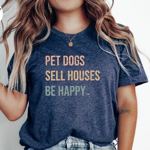 a woman wearing a realtor t - shirt that says pet dogs sell houses be happy