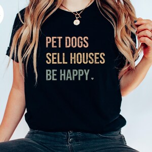 a woman wearing a realtor t - shirt that says pet dogs sell houses be happy