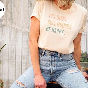 a woman wearing a realtor t - shirt that says pet dogs sell houses be happy