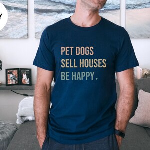a woman wearing a realtor t - shirt that says pet dogs sell houses be happy