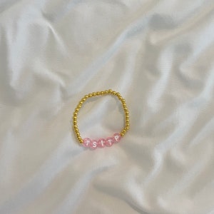 May include: A gold beaded bracelet with pink beads that spell out "TSITP".