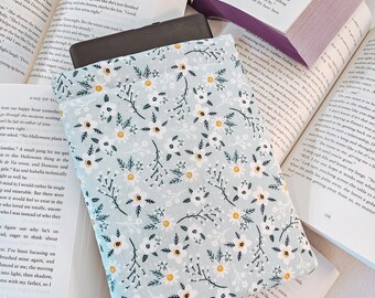 May include: A light blue fabric book sleeve with a white daisy and green leaf pattern. The sleeve is folded and placed on top of two open books.