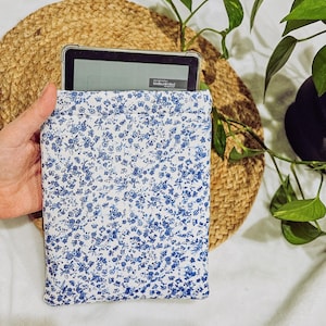 May include: A white and blue floral patterned fabric pouch with a black e-reader inside. The e-reader screen displays the text "kindle unlimited".