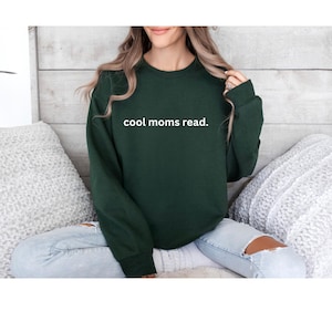 May include: A dark green sweatshirt with the text "cool moms read." in white. The crew neck sweatshirt is a solid color and has long sleeves. The sweatshirt is a casual style.