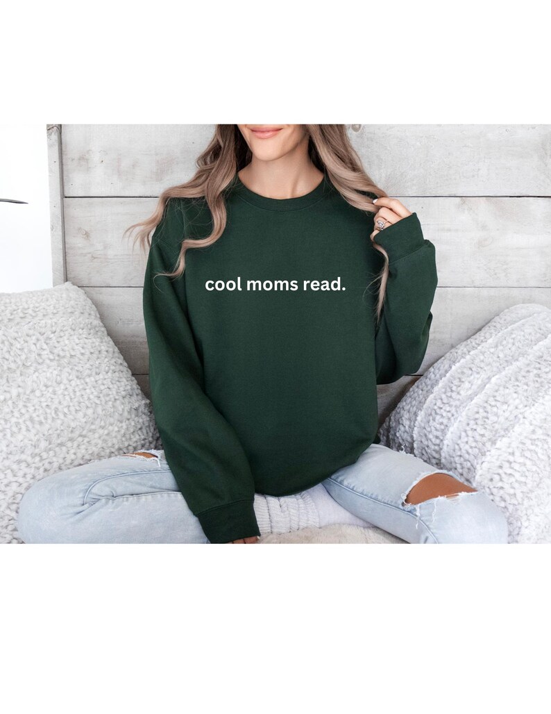 May include: A dark green sweatshirt with the text "cool moms read." in white. The crew neck sweatshirt is a solid color and has long sleeves. The sweatshirt is a casual style.
