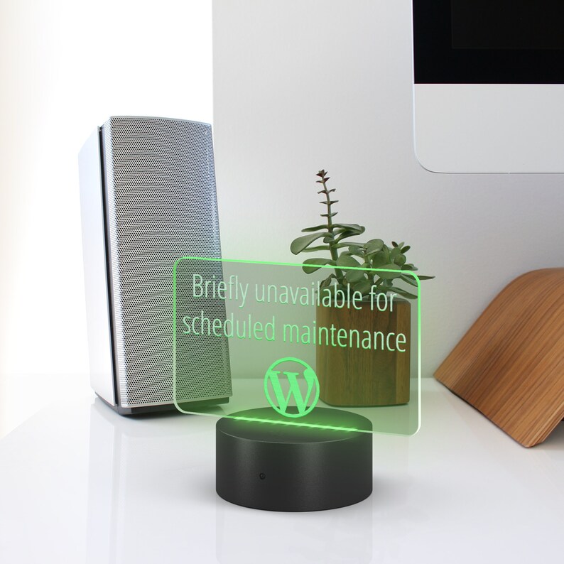 May include: A green illuminated sign with the text "Briefly unavailable for scheduled maintenance" and the WordPress logo. The sign is on a black base and is sitting on a white surface.