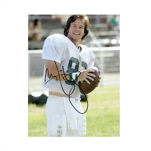 May include: A white football jersey with green trim and the number 88 on the front. The jersey is worn by a man with brown hair and a beard. He is holding a brown football in his right hand. The background is a green field.