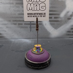 May include: A unique card holder made from a purple spray paint can base, holding a white card with the word "MAG" repeated three times. The card also displays the website address and the words "Mixed Media & Pop Art".