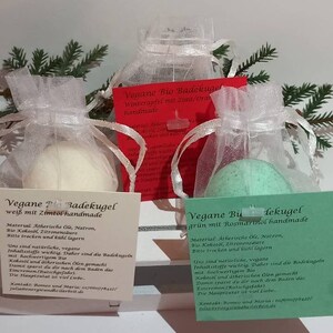 Può includere: Tre bombe da bagno vegane in sacchetti di rete bianca, verde e rossa. Le bombe da bagno sono etichettate con il testo "Vegane Bio Badekugel" e le fragranze "weiß mit Zimtöl handmade", "grün mit Rosmarinöl handmade" e "Winterapfel mit Zimt/Orange handmade".