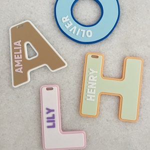 May include: Four personalised name tags with different colours and fonts. The names are Amelia, Oliver, Henry, and Lily.