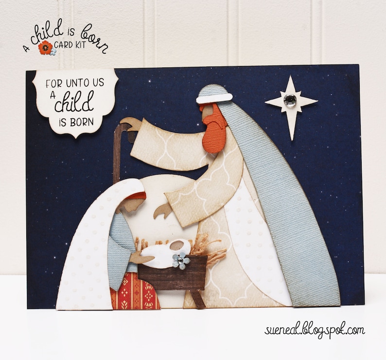 May include: A Christmas card kit with a blue background and a white, red, and brown paper cut-out of the nativity scene. The text "For unto us a child is born" is on the card.