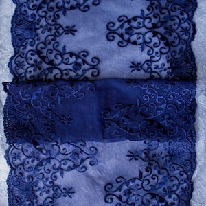 Puede incluir: Primer plano de una tela de encaje azul marino con intrincados patrones florales y de volutas. El encaje tiene un borde festoneado y est&aacute; superpuesto a una tela azul m&aacute;s clara, creando un contraste de color y textura. El dise&ntilde;o es sim&eacute;trico y detallado.