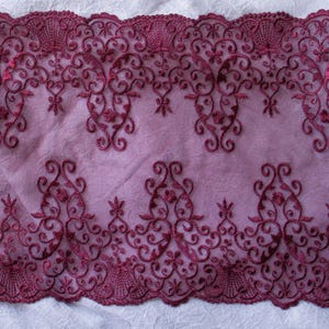 Puede incluir: Tela de encaje burdeos con un intrincado dise&ntilde;o floral y de volutas. El encaje presenta un borde festoneado y est&aacute; sobre un fondo lavanda suave. El bordado detallado crea una textura delicada y elegante, adecuada para diversos proyectos de manualidades.