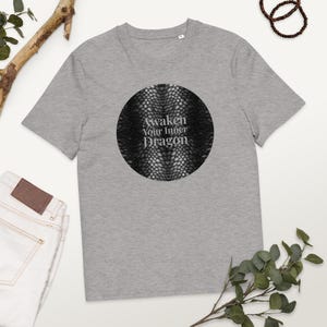 Könnte beinhalten: Graues T-Shirt mit einem kreisförmigen Design mit strukturiertem Muster und dem Text "Awaken Your Inner Dragon". Das T-Shirt besteht aus einem weichen Material und hat einen klassischen Rundhalsausschnitt.