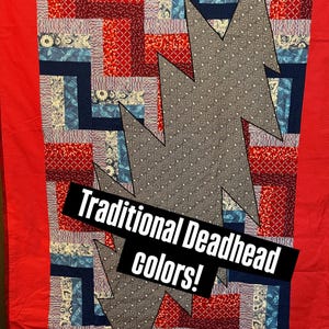 Könnte beinhalten: Ein Patchwork-Quilt mit rotem Rand und einem zentralen Design mit einem grauen Blitz. Der Quilt enthält rote, blaue und gemusterte Stoffe. Der Text "Traditional Deadhead colors!" wird auf einem schwarzen Banner angezeigt.