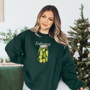 Op de afbeelding: Een donkergroen sweatshirt met de tekst "Enthusiast" en een afbeelding van een pot vol groene augurken.