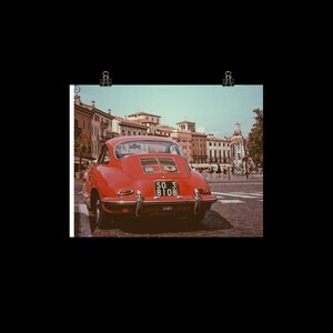 May include: A red vintage Porsche 911 driving through a European city street. The car has a license plate that reads "SO 3 8108".