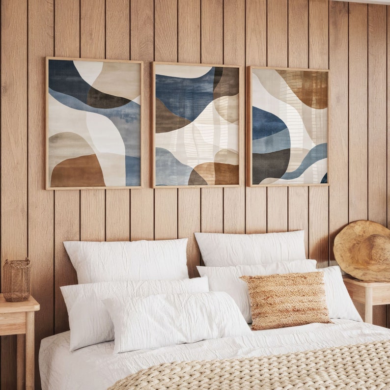 Pode incluir: Tr&ecirc;s impress&otilde;es de arte abstrata com um esquema de cores marrom, azul e branco. As impress&otilde;es s&atilde;o emolduradas em madeira natural e penduradas em uma parede de madeira.