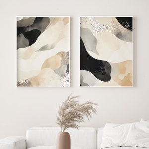 Op de afbeelding: Twee abstracte kunstprints in witte frames. De prints tonen een beige, grijs en zwart aquarelontwerp met een gespikkeld patroon.