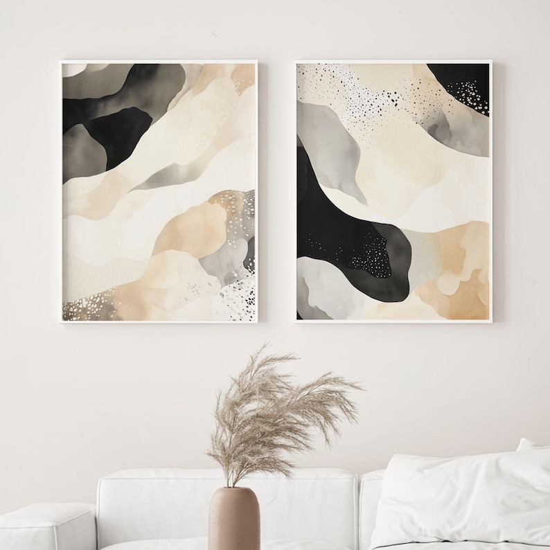 Op de afbeelding: Twee abstracte kunstprints in witte frames. De prints tonen een beige, grijs en zwart aquarelontwerp met een gespikkeld patroon.