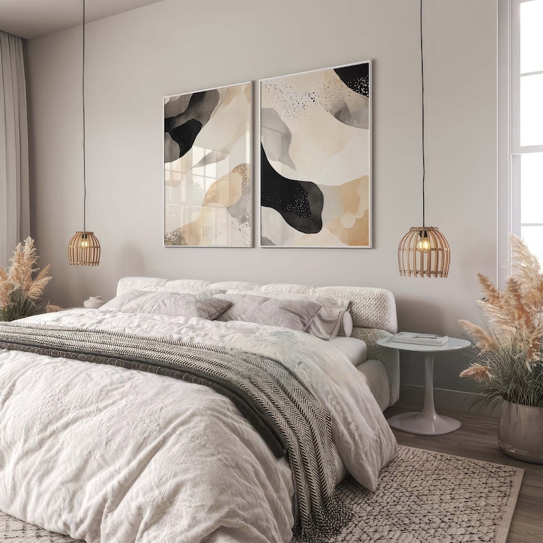 Op de afbeelding: Een slaapkamer met een wit bed, een wit en grijs gestreept deken en twee zwart-witte abstracte schilderijen aan de muur. Er hangen twee hanglampen met gevlochten lampenkappen.