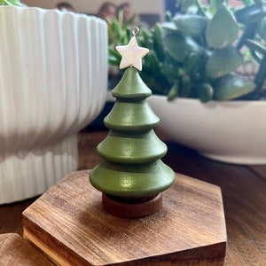 May include: A small green wooden Christmas tree ornament with a white star on top. The tree is sitting on a wooden base.