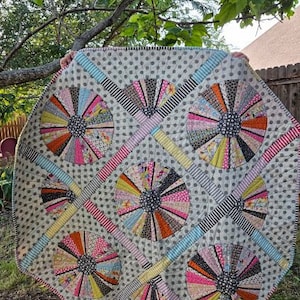 May include: A white quilt with a gray polka dot pattern and a design of colorful pinwheels. The pinwheels are made of different fabrics and colors, including pink, blue, green, and yellow.