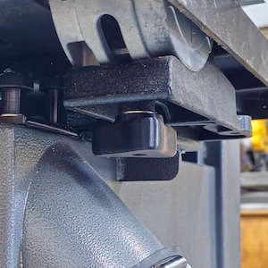 May include: Close-up of a black metal table saw with a gray cast iron table and a black plastic knob. The saw is tilted at an angle and the table is visible in the background.